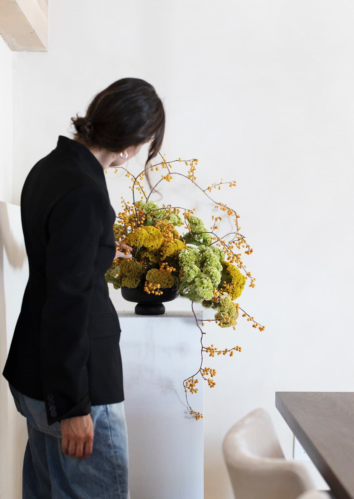 Bloomiér florist finishing a sculptural arrangement of celosia, hydrangea and bittersweet on a plinth in a Vancouver space