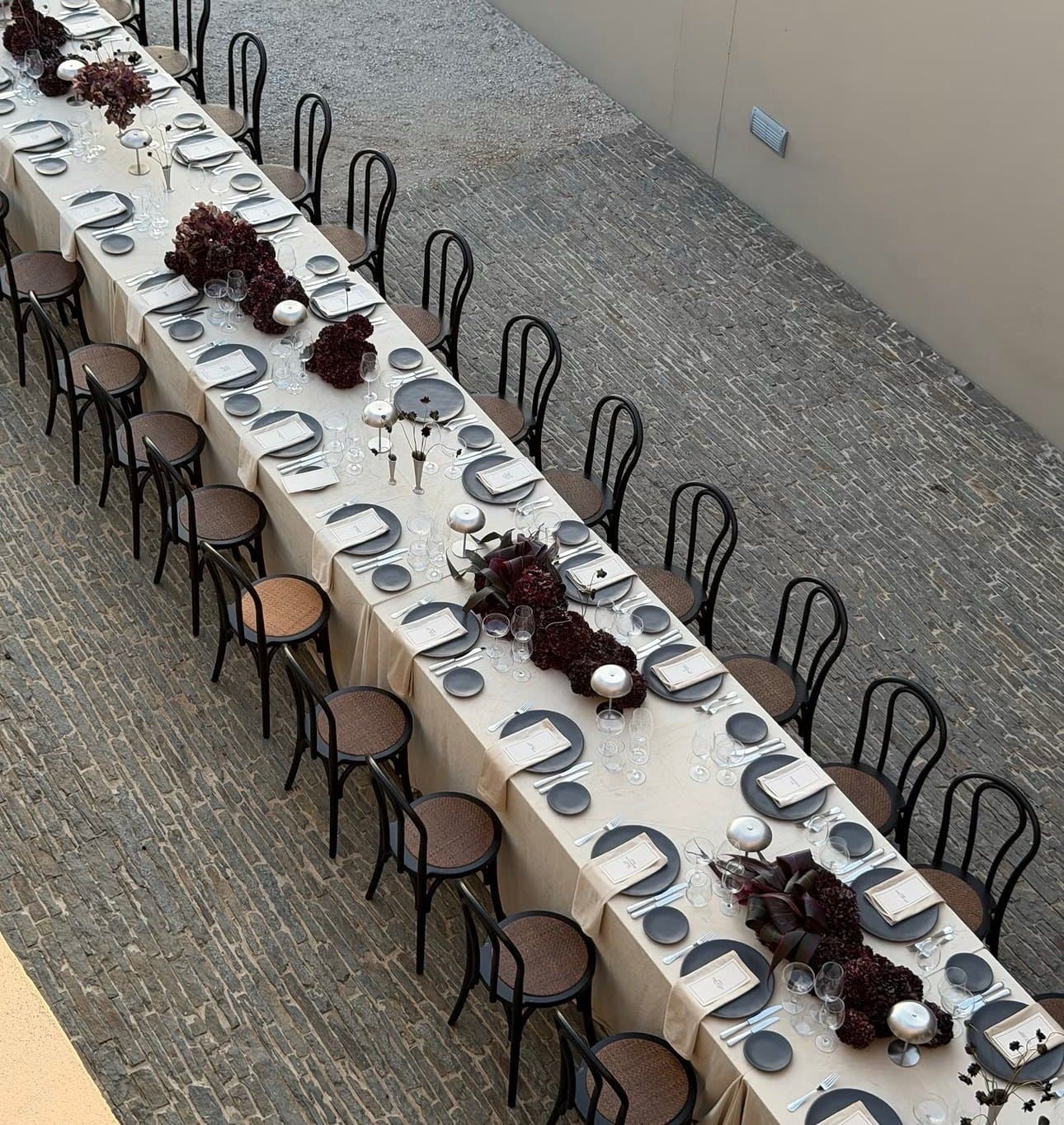 Long banquet table dressed with a runner of deep burgundy blooms and foliage by Bloomiér